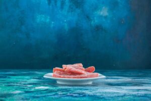 Slices of pink, frozen meat on a white plate against a vibrant blue textured background.