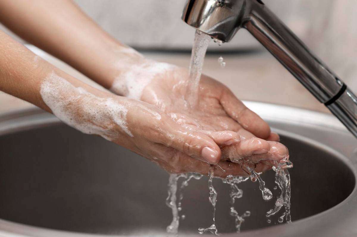 Hands lathered with soap are rinsed under running water from a faucet, emphasizing proper hand hygiene.