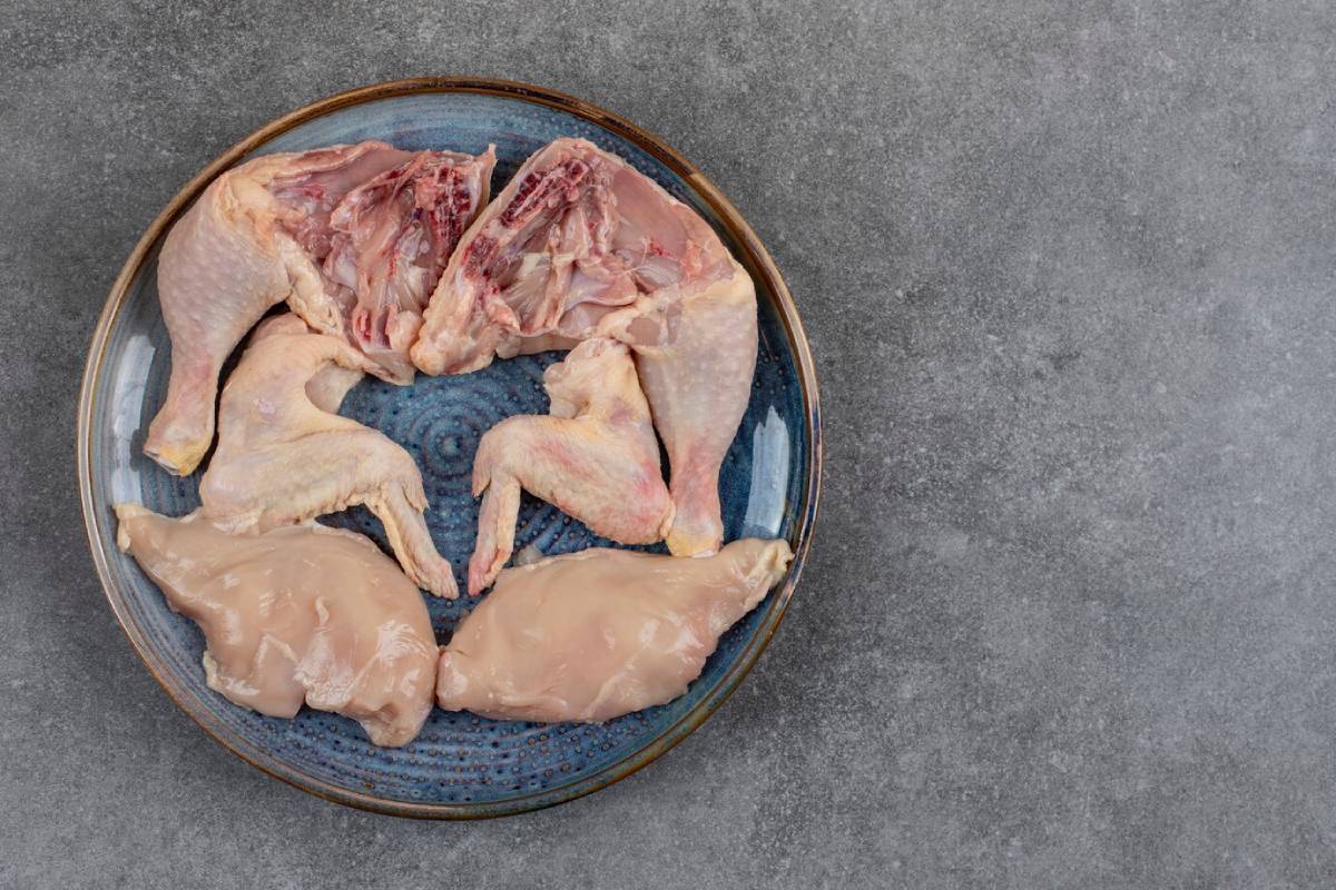 Raw chicken parts, including wings and breasts, arranged on a blue decorative plate against a textured gray background.