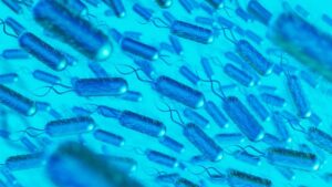 A microscopic view of blue bacteria with flagella, appearing to swim through a vibrant turquoise background.
