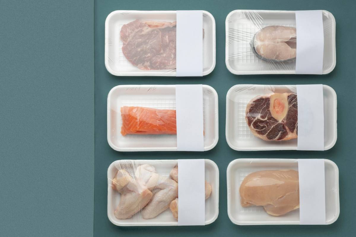 Assorted packaged meats including beef, salmon, chicken wings, and fillets, neatly arranged on a teal background.