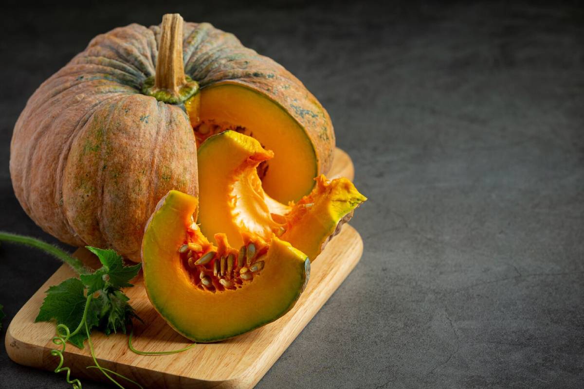  A halved pumpkin rests on a wooden cutting board, showcasing its bright orange flesh and seeds against a dark background.