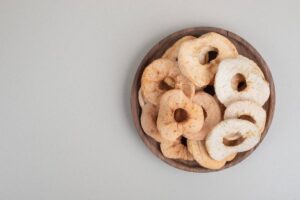 A wooden bowl filled with assorted dried apple rings, showcasing various shades of beige and cream against a light background.