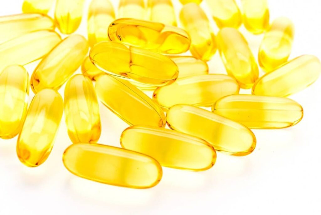 A close-up of translucent yellow softgel capsules scattered on a white background.