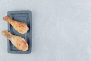 Two golden-brown chicken drumsticks on a black rectangular plate against a light gray background.