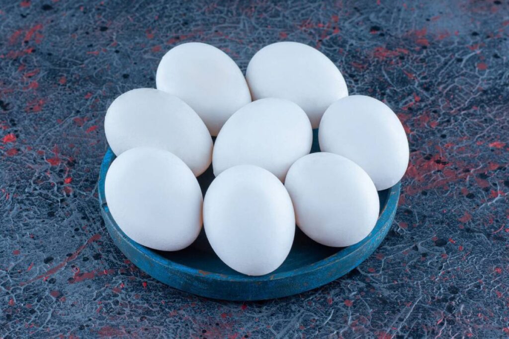 A blue plate holds eight smooth, white eggs against a textured, dark background with red and gray patterns.