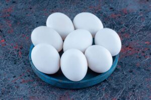 A blue plate holds eight smooth, white eggs against a textured, dark background with red and gray patterns.