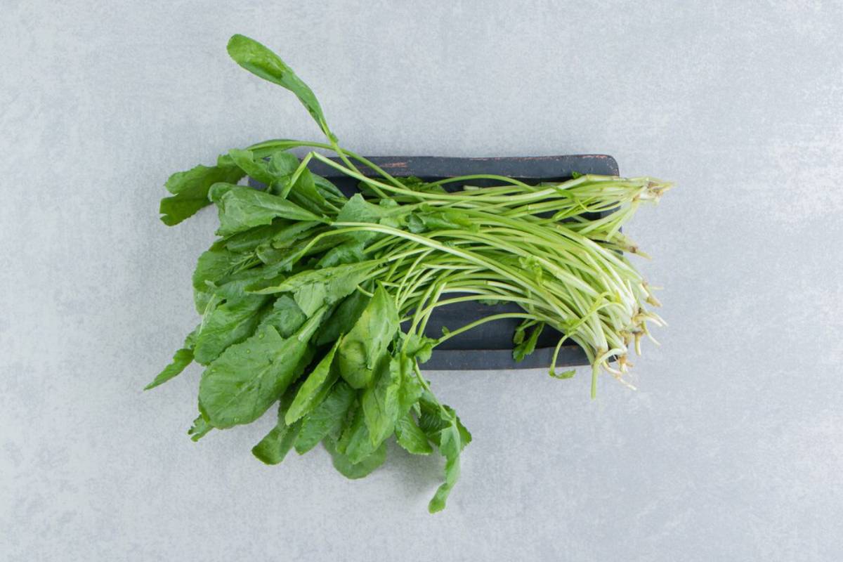 Fresh green spinach leaves atop a dark wooden tray, arranged neatly against a light gray background.