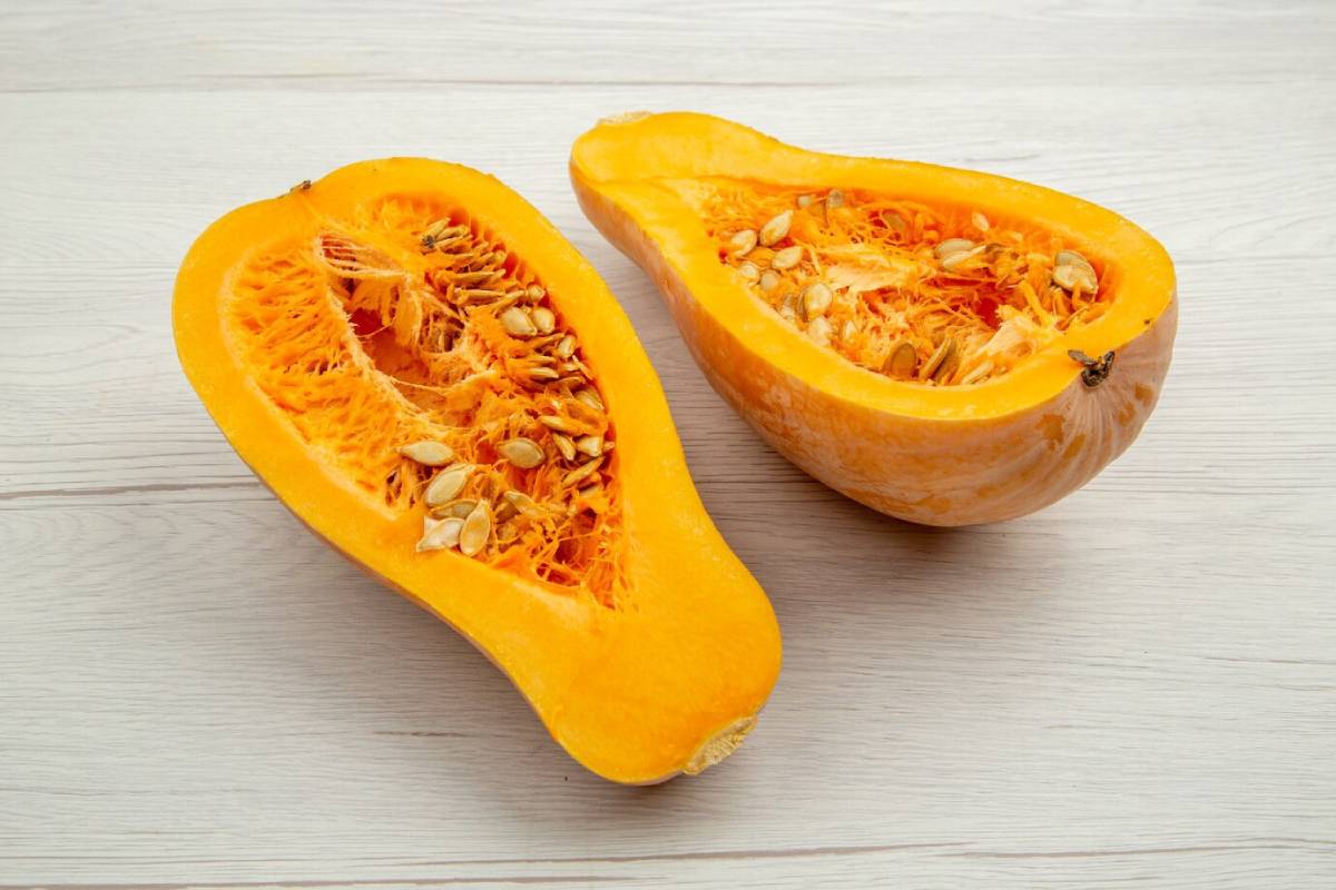 A freshly cut butternut squash, revealing vibrant orange flesh and seeds inside, placed on a light wooden surface.