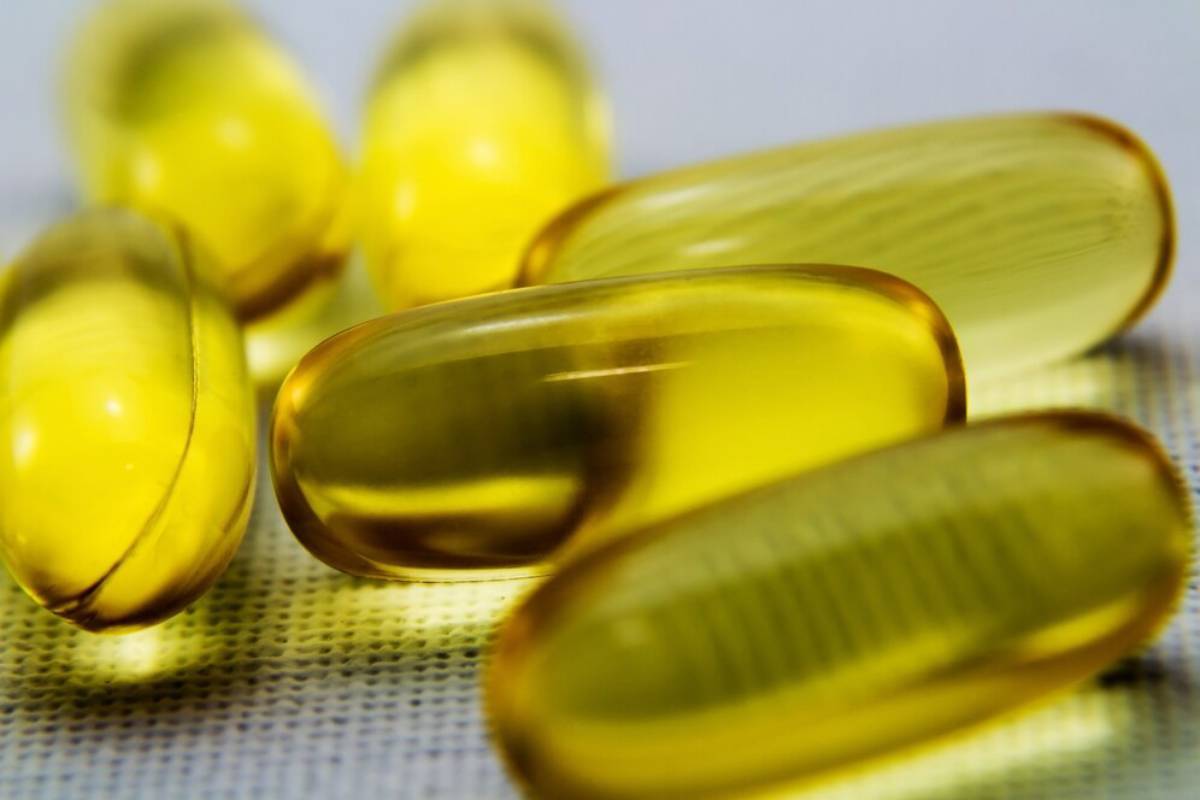 A close-up of translucent yellow omega-3s capsules scattered over a textured white surface, featuring varying shapes and sizes.