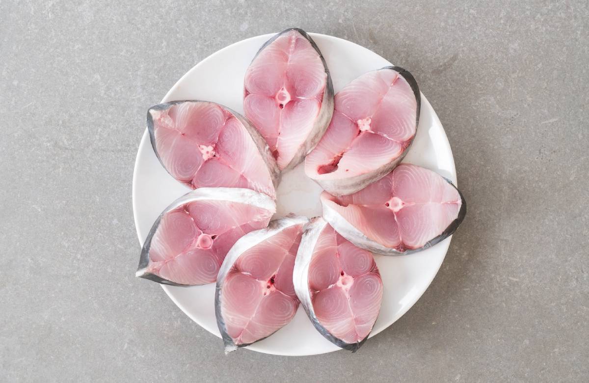A white plate holds several pink fish steaks arranged in a circular pattern, showcasing their fresh, cut surfaces.