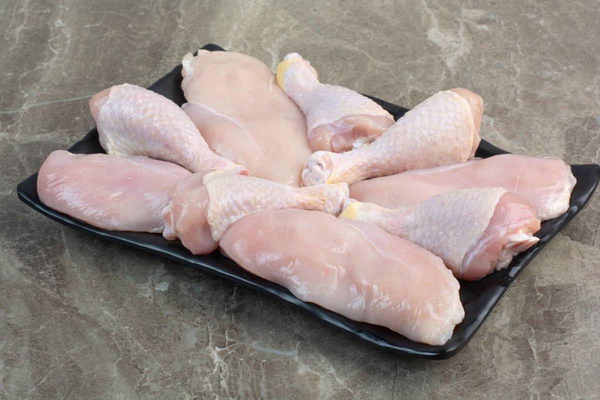 A black platter holds an assortment of raw chicken parts, including drumsticks and chicken breasts, on a marble countertop.