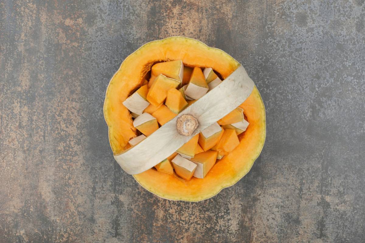 A top view of a halved pumpkin filled with orange and cream-colored cubes, surrounded by pale green pumpkin skin.
