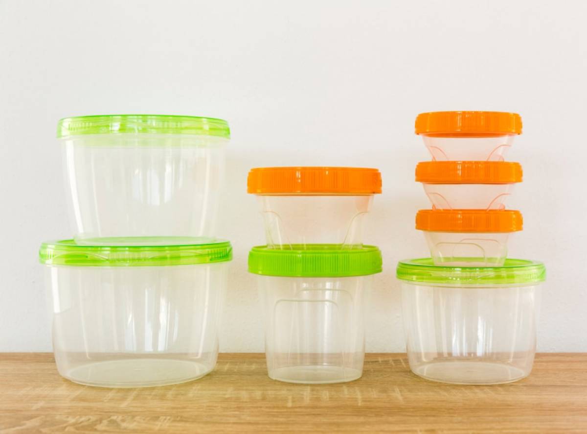 A variety of clear plastic storage containers with green and orange lids, stacked on a wooden surface against a white wall.