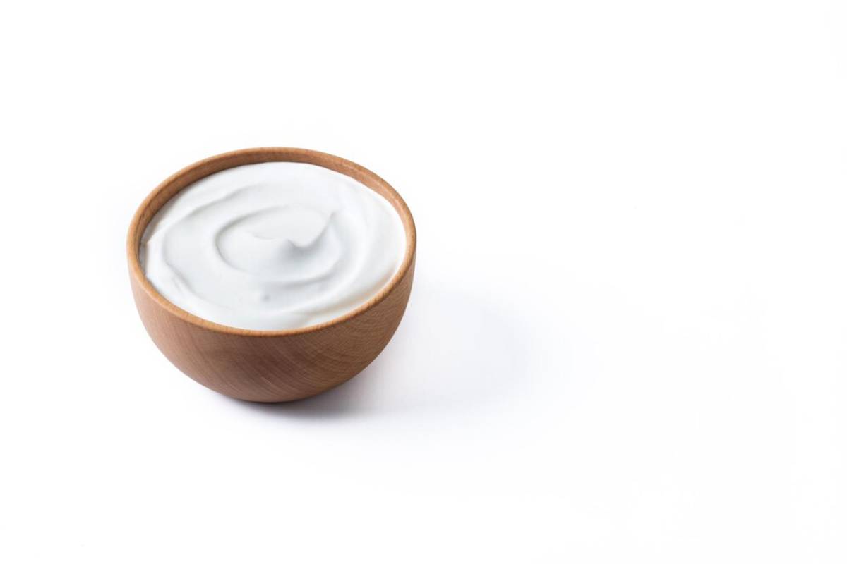 A wooden bowl filled with smooth, creamy yogurt, set against a clean white background. 