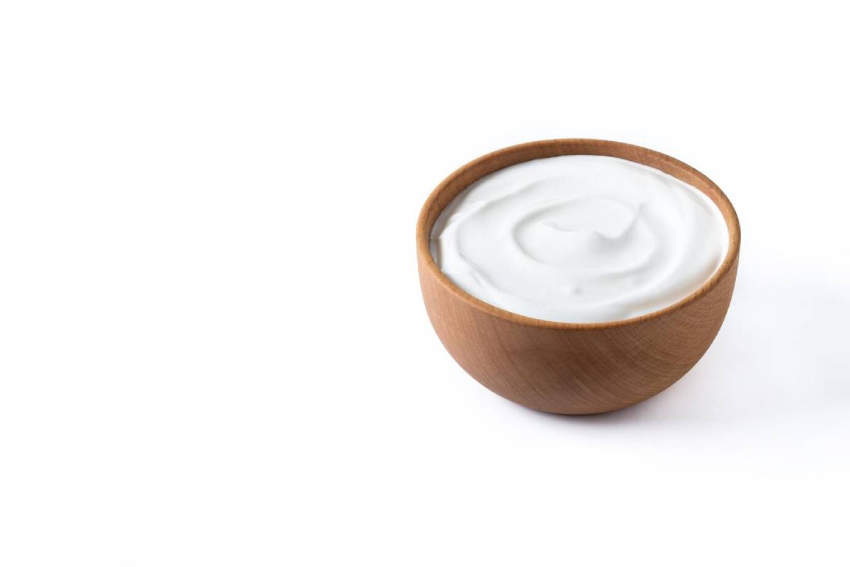 A wooden bowl filled with creamy white yogurt, displayed against a clean white background. 