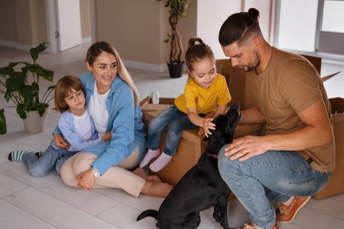  A family of four with a dog sits together on the floor amidst moving boxes, enjoying a moment of joy in their new home.