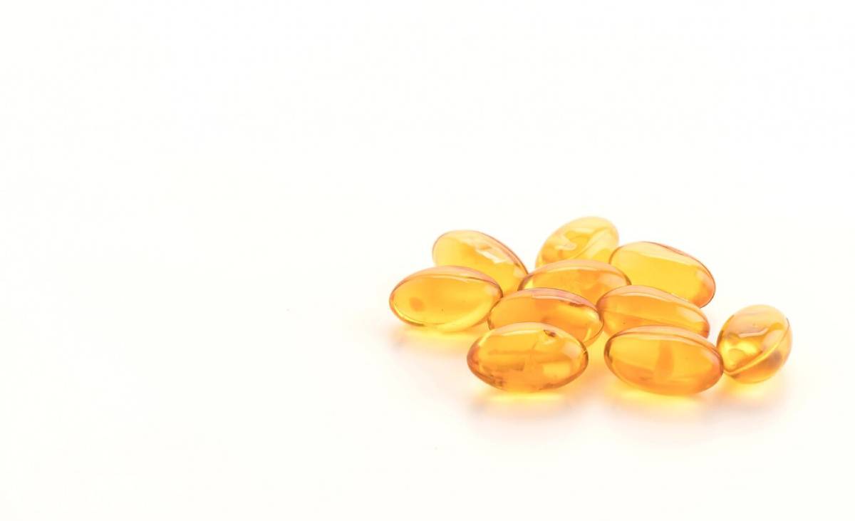 A handful of shiny, orange gel capsules scattered on a light background, representing dietary supplements or vitamins.