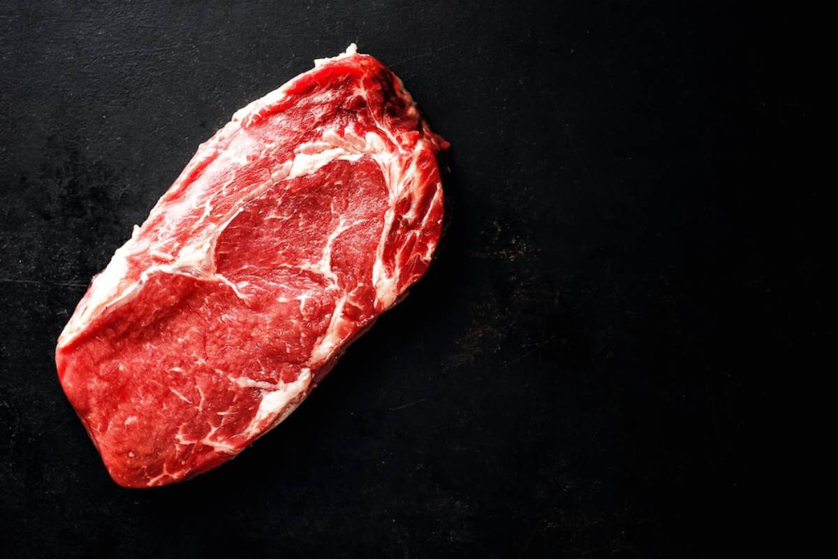 Fresh cut of marbled beef steak on a dark countertop, showcasing rich red and white fat intrusions. Ideal for grilling or roasting.